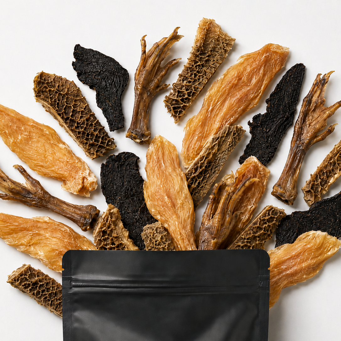 A variety of dried and cured mushrooms, including sliced tan morels, dark black morels, and brown truffles, arranged in a fan shape above an open black resealable pouch on a clean white background.